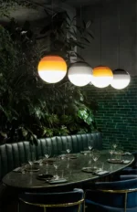 Pink glass pendant lamp shown from an angle, with a blurred background of a restaurant.