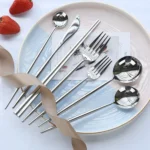 Elegant stainless steel flatware set with forks, spoons, and knives arranged on a wooden table