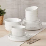 Elegant ceramic plates set with dinner plates, dessert plates, cereal bowls, and soup bowls arranged on a wooden table