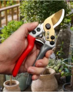 Goldoma pruning shears on a stone pathway with fallen leaves around.