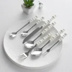 Stainless steel flatware set with ceramic pearl handles on wooden table