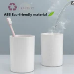 Toothpaste dispenser and toothbrush holder set in a minimalist bathroom, with natural light and plant.