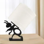 Ant toilet paper holder placed on a wooden living room side table next to a coffee mug and books.