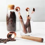 Set of stainless steel measuring cups with copper and rose gold finishes on wooden stand