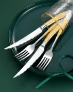 Elegant gold flatware set with steak knife, fork, and spoon on a dark table