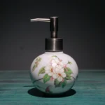 White ceramic toothbrush holder with flowers, on glass bathroom shelf, with towel.
