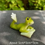 Frog seesaw playground miniature, with a tiny frog on each end, on a patch of artificial grass.