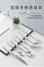 Stainless steel flatware set with ceramic pearl handles on wooden table