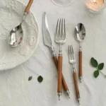 Elegant stainless steel dinnerware set with wooden handles on a rustic table