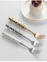 Stainless steel flatware set with ceramic pearl handles on wooden table