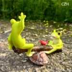 Frog seesaw ornament from low angle, emphasizing height of seesaw, with blurred garden background.