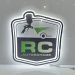 Backlit acrylic sign with a blue logo, displayed on a white wall next to a framed photo.