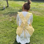 Woman wearing a cotton apron for baking with fresh plaid pattern and ruffled edges in a rustic kitchen