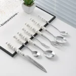 Stainless steel flatware set with ceramic pearl handles on wooden table