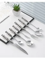 Stainless steel flatware set with ceramic pearl handles on wooden table
