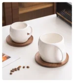 Elegant ceramic coffee mug set with saucer on wooden table, featuring oat-colored cups
