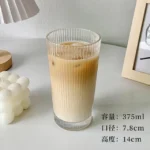 Set of transparent glass coffee mugs with lids and straws on a wooden table