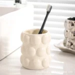 Gold electroplated ceramic cup with a toothbrush and a tube of toothpaste, on a white sink.
