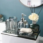 Glass lotion bottle with gold pump, against white tile wall.