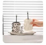 Set of two electroplated ceramic mugs on a bathroom vanity, one with a toothbrush, the other with a razor.