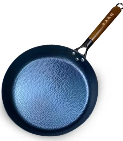 Goldoma uncoated cast iron skillet with hand-hammered surface cooking steak on gas stove