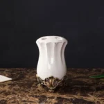 White porcelain lotion bottle with a delicate floral pattern, set on a wooden shelf.