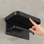 Aluminum toilet paper holder with shelf, displaying a roll and a small air freshener.