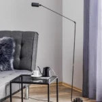 Floor lamp with black metal body and white inner shade, casting warm light in a bedroom corner.