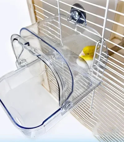 Clear bird bath tub mounted on parakeet cage with bird bathing inside