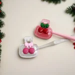 White ceramic toothbrush holder with cherry design placed on bathroom sink, with toothbrush inside.