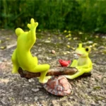 Overhead shot of frog couple on seesaw, showing green and orange colors, on a bed of pebbles.