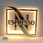 Round acrylic sign with a black logo and cool white backlight, on a glass desk.