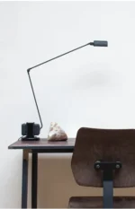 Black lamp with a slim profile, contrasting with a white wall in a bright room.