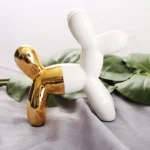 Ceramic balloon dog statue with a slot on top for saving coins, on a desk.
