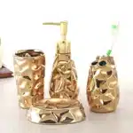 Goldoma four-piece bathroom set including lotion bottle, soap dispenser, toothbrush holder, and cup, arranged on glass
