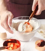 Set of stainless steel measuring cups with copper and rose gold finishes on wooden stand