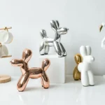 Gold standing balloon dog sculpture on a wooden table with a plant in background.