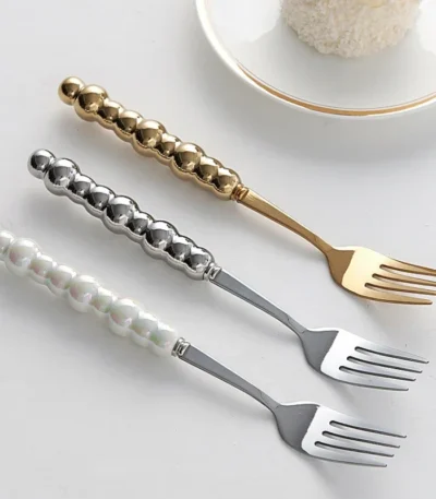 Stainless steel flatware set with ceramic pearl handles on wooden table