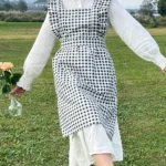 Woman wearing a cotton apron for baking with fresh plaid pattern and ruffled edges in a rustic kitchen