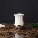 Close-up of a white porcelain toothbrush holder with floral embossing and gold accents.