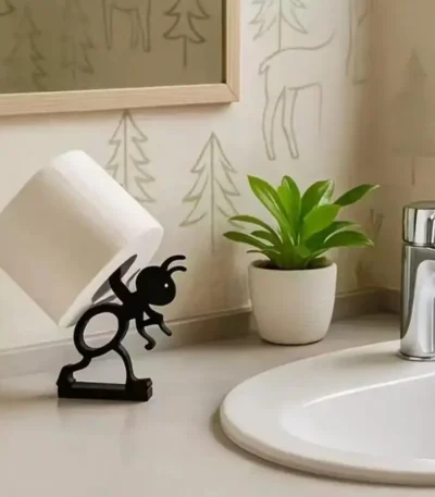 White 3D printed ant toilet paper holder on a bathroom vanity with marble countertop and a small plant.