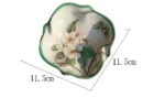 Set of floral ceramic bathroom accessories on wooden shelf, toothbrush holder, cup, lotion bottle.