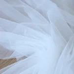 Sheer white wedding arch draping fabric elegantly draped over a wooden arch at an outdoor ceremony