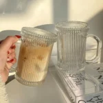 Set of transparent glass coffee mugs with lids and straws on a wooden table