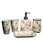 Bathroom accessories set: toothbrush holder, cup, and lotion bottle, all floral ceramic, on white sink.