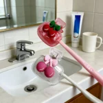 Close-up of cherry pattern on white ceramic toothbrush holder, showing red cherries and green leaves.
