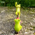 Frog seesaw figurine placed on a shelf with mini plants, showing scale and craftsmanship.