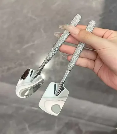 Two stainless steel ice cream spoons with ergonomic handles, one scooping a bowl of vanilla ice cream