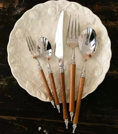 Elegant stainless steel dinnerware set with wooden handles on a rustic table