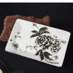 Soap dish with a ceramic texture and floral design, placed next to a soap bar on a wooden shelf.